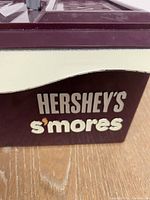 Side view showing Hershey's S'mores branding in white and tan on chocolate brown and cream colored plastic box.
