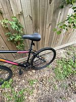 Side view of the black Northline Trail mountain bike showing rear wheel, seat, and part of frame with red and orange accents near a wooden fence.