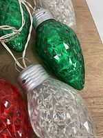 Close-up photo showing the textured green and clear oversized Christmas light bulbs with silver caps on a white wire.