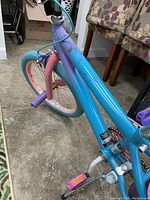 Close-up photo of the blue frame bike with pink fork and blue tire with pink rim, purple pedal and front peg for stunts