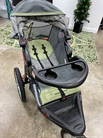 Full view of the green and gray running stroller showing seating, harness, and canopy.