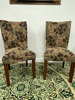 Pair of two cushioned chairs side by side showing full front view with patterned upholstery and wooden legs on patterned rug.
