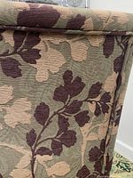 Close-up of the floral tapestry fabric upholstery showing detailed leaf pattern in purple and beige on green background.