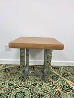 Side view showing thick wood top and polished stainless steel legs with geometric design