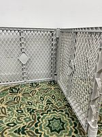 Front view of the three-panel plastic safety gate arranged on a patterned carpet against a white wall.
