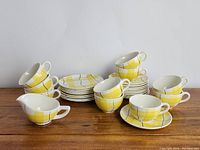 Full view of cups, saucers, small plates, and creamer arranged on table showing yellow plaid pattern and shapes of items.