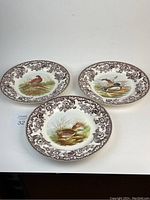 Three Spode Woodland decorative dinner plates laid out to show front design of different game birds: mallard, quail, pheasant.