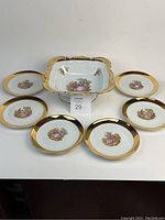 Full view of the serving bowl surrounded by six plates showing the Bavarian couple illustrations and gold rims.