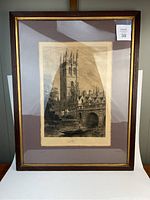 Full view of the large framed etching of a gothic tower and bridge in black and white, shown on a white surface, revealing frame and matting