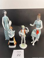 Four Hollohaza porcelain figurines shown together on black background, including tall woman with vase, seated woman with chili peppers, woman in folk dress, and small man figure.