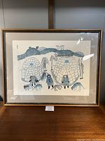 Full view of framed Inuit print showing two igloos, several Inuit figures in parkas, sled dogs and hunting tools.
