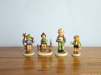 Front view of the four Goebel child figurines displayed on a wooden surface against a light background.