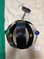 Full view of the hanging swag lamp made of black metal bands with colorful Lucite spheres attached, hung by a chain and ceiling plate