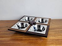 Top-angle photo showing the two-toned wooden lazy susan with four steel removable bowl inserts arranged in quadrants.