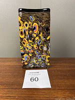 Front view showing the dense millefiori floral glass pattern with yellow, blue, and orange colors on a dark background with reflective glass embedded.