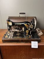 Full side view of the Singer Model 128 sewing machine with bentwood carrying case in background, showing the ornate decals and electric cords.