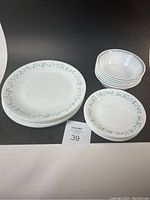 Photo showing stacked white plates and bowls with floral border design, including 8 dinner plates, 7 side plates, and 6 bowls.