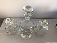 Front view of three clear glass decanters with stoppers, showing their varying shapes and sizes.