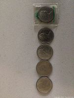 Five Canadian 1 dollar coins arranged in a vertical line on a white background, one coin in a plastic sleeve.