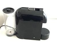 Side view of black Nespresso D50 coffee machine with clear cylindrical water tank and drip tray visible.