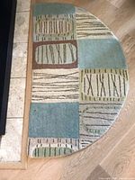 Semi-circle rug with geometric shapes and various colors placed on wood floor next to stone floor border.