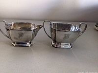 Front angle view of the silver sugar and cream set showing the monogram engraving on each item.