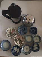 Top-down photo showing the Bodum glass tea pot, silver teapot, and 10 blue and white appetizer dishes arranged on a cream surface.