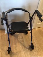 Front view of a blue Drive walker with black padded seat and handle grips, showing the frame, wheels, and seating area.
