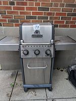 Front view of Baron propane BBQ grill showing stainless steel body, three control knobs, and built-in thermometer on lid.