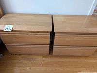 Pair of matching light wood nightstands with two drawers each, photographed against a white wall and hardwood floor.