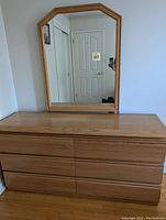 Front view of the wooden dresser with six drawers and attached mirror showing the medium wood finish and rectangular shaped mirror with matching frame.