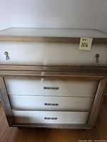 Photo of white 4 drawer dresser with brown trim, showing the front of the dresser with metal handles on each drawer.