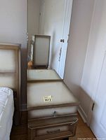 Photo of two beige tone wooden nightstands with drawers and matching mirror resting on one of the nightstands.