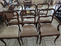 Six wooden dining chairs arranged in two rows; five standard chairs and one captain's chair.