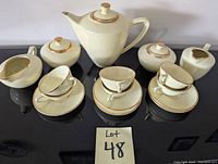 Full view of cream-colored china tea set including teapot, two creamers, two sugar bowls, six cups, and five saucers arranged on black surface.