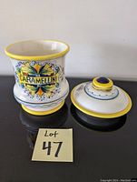 Two-piece China cookie jar: a jar body labeled 'Caramellini' with colorful decorative floral motifs and a matching lid with a decorative knob, shown removed from the jar.