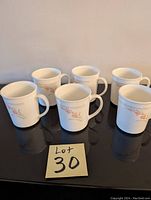 Six white CorningWare mugs with orange and beige floral pattern, arranged on a black reflective surface.
