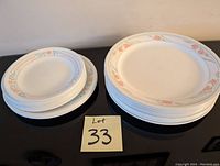 Photo shows a set of 12 Corningware plates divided into two stacks, larger dinner plates on the right and smaller dessert plates on the left, each decorated with a beige rim and peach and light blue floral design.