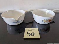 Photo showing two CorningWare pots, one with blue floral design and pouring spout, the other with vegetable design.
