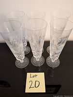 Six clear crystal parfait glasses with pinwheel cut pattern, arranged in a group on a reflective black surface with a lot number card '20' in front.