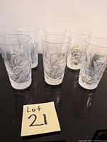 Photo of six clear crystal tumblers with an intricate pinwheel cut pattern set on a dark reflective surface.