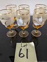 Photo showing six crystal wine/liquor glasses with gold trimmed rims and bases, and white painted leaf decoration on the bowl, arranged in two rows.