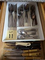 Photo showing the assorted cutlery in a divided plastic tray and knives laid below the tray in a drawer.
