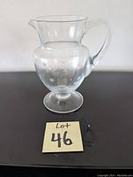Photo of a clear glass decanter with handle and etched star and snowflake designs on the body, displayed on a dark surface with note marked 'Lot 46'.