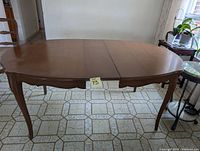 Wooden rectangular dining table with rounded ends, carved edges, and cabriole legs, shown in a tiled room.