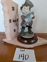 Photo of ceramic figurine of boy holding fish beside stone clock on wooden base