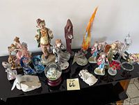 Image showing a table with an assortment of 18 figurines including clown, gnome, cloaked figure, dolphins, swan, snow globe, and other decorative pieces.