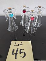 Photo of four glass angel figurines approximately 4 inches tall, each with clear glass wings and halos and colored heart decorations in front, set on a black surface.
