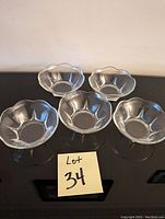 Set of five clear glass bowls with scalloped edges arranged on a black surface next to a label reading Lot 34.
