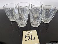 Photo shows six clear textured glasses arranged in two rows on a reflective surface, labeled with lot number 56.
